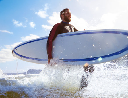 Low angle, surfer or man happy with surfboard, fitness or travel for water sport at the beach. Male person, surfing with view or thinking outdoor, exercise and adventure in nature with ocean splashの写真素材