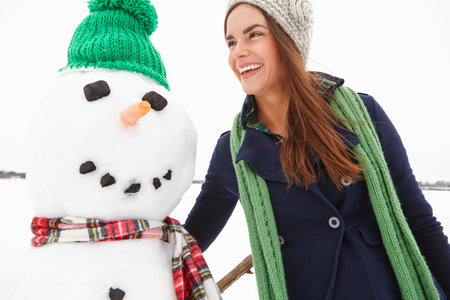 Winter, woman and laughing with snowman outdoor for travel adventure, creative expression or fun. Holiday season, person and happy with snow figure in cold weather for festive activity or funny tripの写真素材