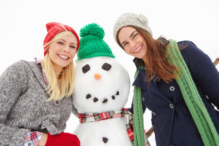 Women, friends and snowman in portrait, happy and bonding with fun, hug or winter holiday. People, smile and cold weather with break, vacation and playful with sweater with excited in Switzerlandの写真素材