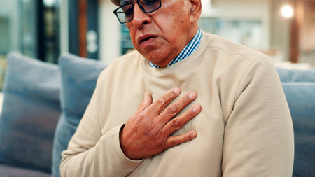 Senior man, chest pain and sofa with heart attack for cardiac arrest, illness or disease in home. Elderly, male person or hypertension with sore cough, respiratory infection or high blood pressureの写真素材