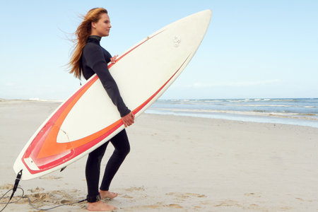 Surfboard, beach and woman by ocean for holiday, vacation or getaway in summer with adventure. View, space and female person with surfing for fitness, exercise or water sports on weekend trip.の写真素材