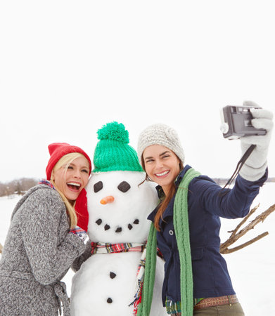 Women, friends and selfie with snowman, happy and bonding with camera, hug and winter holiday. People, space and photography with cold weather, vacation and embrace sculpture with laugh in natureの写真素材