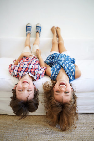 Upside down, relax and kids on couch with portrait, playing and happiness for weekend break and bonding. Children, home and boy with girl in living room together with holiday, vacation and comfortの写真素材