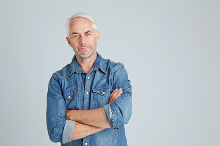 Portrait, man or relax in studio with arms crossed for casual fashion designer, pride or optimism. Confident, mature person or smile on gray background for denim shirt, clothing style or mockup spaceの写真素材