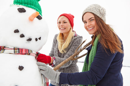 Portrait, friends or building a snowman outdoor for winter adventure, playful fun or bonding. Happy, women and snow figure decoration for holiday activity, funny teamwork or festive traditionの写真素材