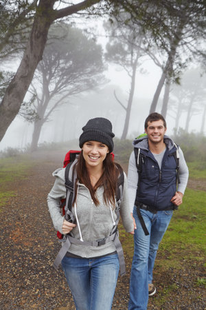Portrait, couple and hiking in woods for fitness adventure, morning fog and trekking on holiday. Smile, people or backpacking journey in forest with mist, explore nature and holding hands on vacationの写真素材