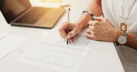 Senior, woman and hands writing with laptop for finance, budget planning or expenses in home. Closeup, female person or checking costs with documents for financial investment or bills in houseの写真素材