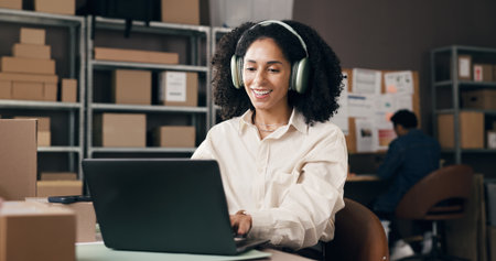 Ecommerce, headphones or black woman in office with laptop, inventory control or music streaming at work. Logistic, song or supplier in agency with tech, radio or podcast subscription in supply chainの写真素材