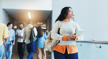 Woman, college student and tablet with thinking, smile and walk in hallway for scholarship at campus. Girl, reflection and tech with bag, app or learning with perspective for education at universityの写真素材