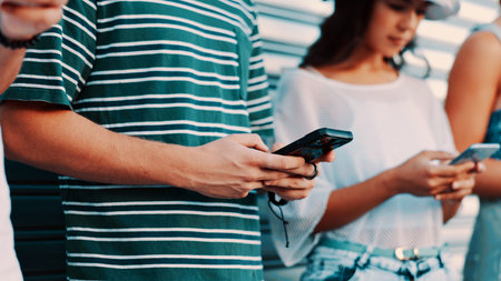 Hands, phone and text message with friends outdoor together for connection or social media browsing. App, contact and typing with group of people in line for communication, online chat or readingの写真素材