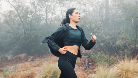 Woman, running and nature with mist for fitness training, cardio exercise or outdoor workout. Active, female person or runner with sprint, race or woods for winter challenge, stamina or enduranceの写真素材