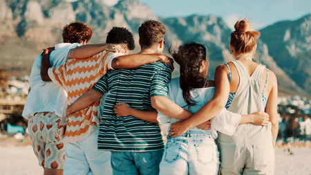 People, friends and back view with hug on beach for summer vacation, bonding or outdoor fun. Group, community or embrace with sunshine on ocean coast for travel, holiday or weekend together in natureの写真素材