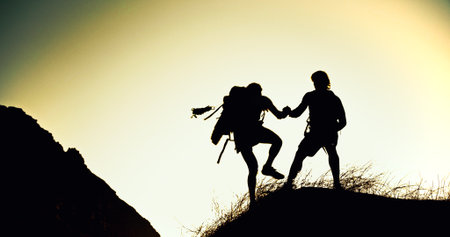 Hiking, silhouette or people on cliff with support, together or motivation for exploration goals. Adventure, journey or friend on mountain with climb, endurance or helping hand for trekking milestoneの写真素材