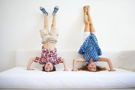 Playful, kids and handstand for fun on sofa for gymnastics, balance and bonding together. Children, siblings and upside down for motor skills, activity and games for weekend entertainment at houseの写真素材