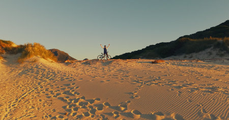 Dune, bicycle and man with celebration for sunset view, travel and fitness for journey with banner. Person, cycling and explore for exercise, eco tourism and nature space for holiday or vacationの写真素材