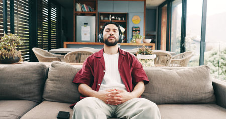 Calm man, relax and sofa with headphones for music, listening or audio streaming in home. Male person, user or sound therapy with song playlist for stress relief, break or rest on couch in houseの写真素材