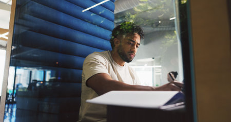 Writing, thinking and businessman in office with notebook for planning creative project in pod. Booth, professional and magazine editor working on article with research for publishing in workplace.の写真素材