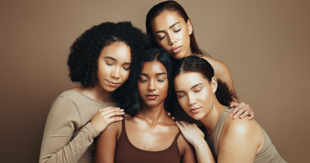Women, eyes closed and diversity in studio for beauty, solidarity and bonding together with hug or unity. Friends, support and inclusion on brown background for love, community or natural dermatologyの写真素材
