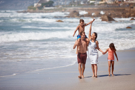Walking, happy and travel with family at beach for bonding, summer vacation and adventure. Support, holiday getaway and care with parents and children outdoor for weekend break, space and loveの写真素材