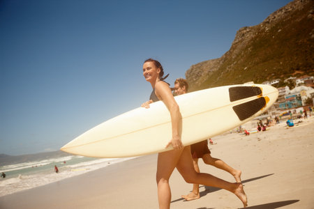 Surfboard, happy and couple on beach for fitness, vacation or weekend trip in summer together. Running, water sports and female person by ocean for travel, getaway or holiday with seaside hobby.の写真素材