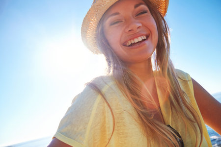 Portrait, smile and woman on beach to relax for travel, holiday and outdoors with space. Flare, summer and happy person with sunshine by ocean for fresh air, vacation and weekend getawayの写真素材