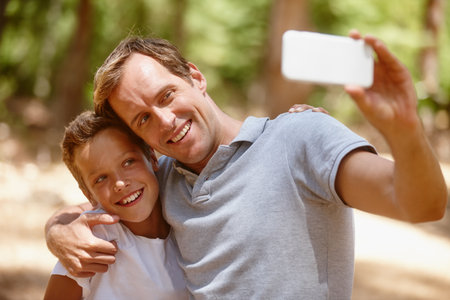 Happy father, son or forest with selfie for picture, photography or outdoor memory together. Dad, child or kid with smile, hug or embrace for capture moment, bonding or family time in nature or woodsの写真素材