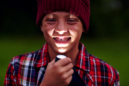 Dark, portrait and child with flashlight for storytelling, fun activity or camping outdoor. Night, boy and torch on chin for reading tale, campsite mystery or play game in nature.の写真素材