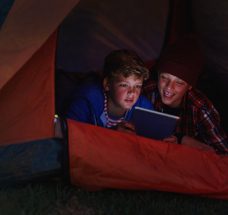 Night, kids outdoor and tablet in tent with smile for playing games, adventure story app and bonding. Late, friends and boys in nature with fort, digital technology and connection for online gaming.の写真素材