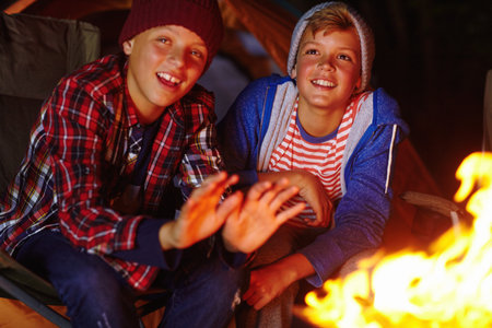 Camp, fire and night with children outdoor together for adventure, bonding or survival hobby. Dark, flame and warm with group of happy kids at campsite for holiday, travel or vacation as friendsの写真素材