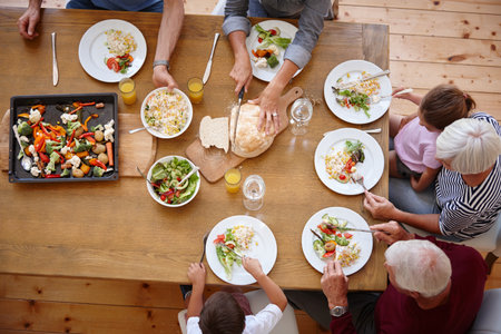 Above, food and hands with family in dining room of home for eating, thanksgiving season and celebration. Festive meal, bonding and reunion with people in house for lunch, holiday and traditionの写真素材