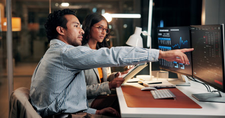 Pointing, meeting and business people on computer at night for finance review, investment and budget report. Office, working late and workers on tech for financial analytics, research or stock marketの写真素材