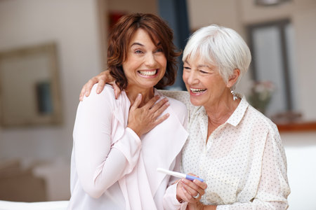 Elderly mom, excited and woman with pregnancy test or sharing good news with old parent in apartment. Happy, family and stick with positive results, embrace and celebration for IVF success in homeの写真素材