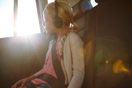 Headphones, window and child in car with road trip, adventure or journey for vacation. Music, reflection and girl with audio in vehicle for holiday, transport or travel with flare for album streamingの写真素材