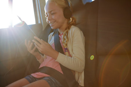 Headphones, tablet and girl with road trip, adventure or journey for vacation in car. Tech, streaming and child with audio in vehicle for holiday, transport or travel with flare for entertainmentの写真素材