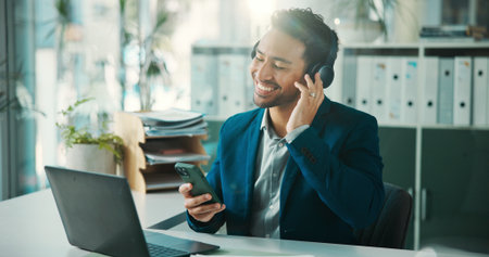 Headphones, happy or man in office with phone, sound track streaming or listening to music at work. Flare, playlist or employee in agency with laptop, podcast or radio subscription on audio app.の写真素材