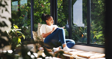 Happy, woman and thinking with notebook, window and writer with ideas for novel or planning in home. Creative, author and black person with journal for story, reflection and smile for remote workの写真素材