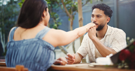 Couple, holding hands and kiss on date at restaurant with bouquet, discussion and relationship milestone. Happy man, woman and connection with bonding, trust and flowers for anniversary at dinerの写真素材