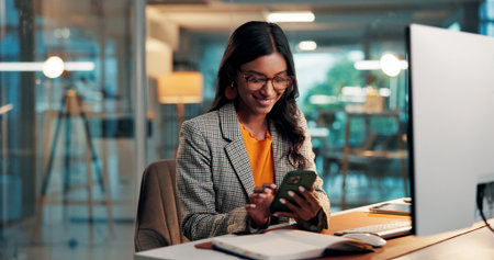 Phone, message and woman with computer in office for creative project overtime with online article. Glasses, draft feedback and magazine editor with evening for review or publishing deadline on techの写真素材