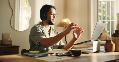 Happy man, video call and laptop with headphones in home for webinar, communication or network. Male person, remote work with computer or app for online meeting, discussion or virtual chat in houseの写真素材