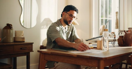 Documents, remote work and writing with man in home office for journalism or publication. Paperwork, pen and planning with freelance journalist at desk in study of apartment for article researchの写真素材