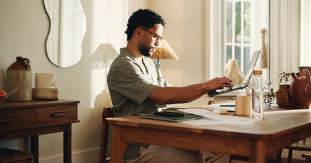 Typing, man and creative with laptop, home and research for logo design on web or freelance project. Graphic designer, online and person with tech for digital art, technical skills and remote workの写真素材