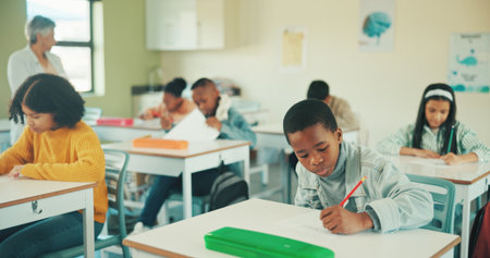 Boy, writing test and learning in classroom at school, assessment and development with scholarship. Child, education and exam paper with problem solving, answer or pupils with evaluation at academyの写真素材