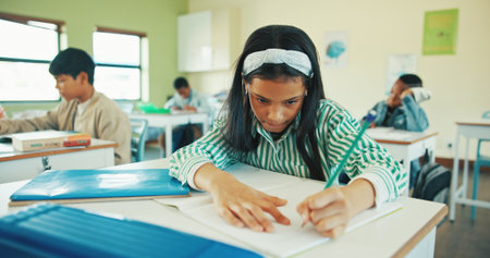 Classroom, writing and child with notebook for learning, development and assessment for education. Knowledge, question solution and girl with pencil for assignment, concentration and problem solvingの写真素材