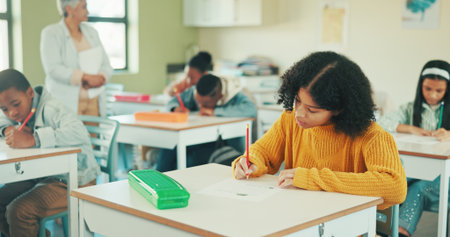 Student, girl and writing in classroom with test for education, learning and skill development. People, child or notes in school with pencil for exam, academic assignment and assessment solution.の写真素材