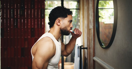 Man, profile or brushing teeth with mirror in bathroom for dental hygiene or fresh breath. Male person, cleaning and grooming with toothbrush or morning routine in home for mouth, oral and gum careの写真素材