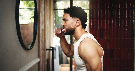 Man, morning and brushing teeth with mirror in bathroom for dental hygiene or fresh breath in home. Profile, male person or cleaning mouth with toothbrush for grooming, oral or gum care in houseの写真素材