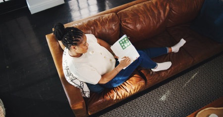 Above, black woman and writing with notebook in living room for planning, schedule or checklist. Home, thinking and journal of freelancer for remote work, copywriting or ideas for article editorの写真素材