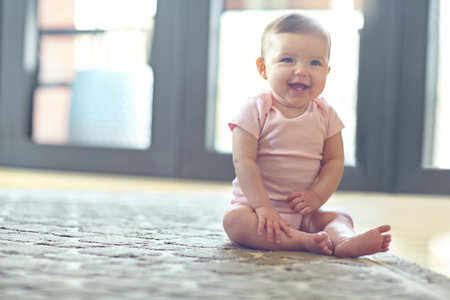Excited, laugh and baby girl in house on floor, balance and growth in infant stage. Wellness, home space and young child in living room with smile, sitting and development milestone in childhoodの写真素材