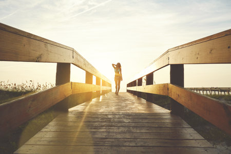 Tourist, sunset or woman on bridge in swimwear, outdoor trip or fresh air on weekend break. Travel, flare or female person in nature with walkway, seasonal getaway or summer evening in Australia.の写真素材