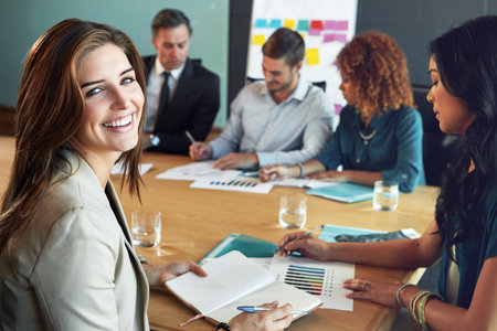 Happy, business people and portrait of woman in meeting for planning, feedback and budget review. Corporate, boardroom and worker with notebook for discussion, strategy or finance report for proposalの写真素材